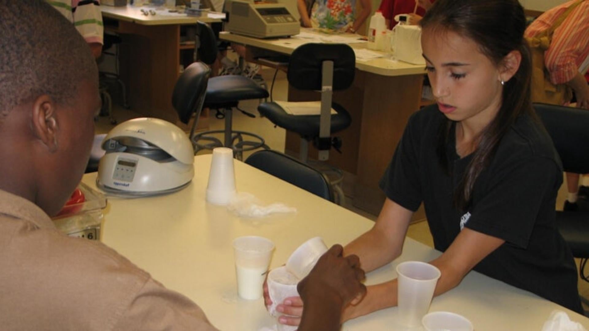 Photo of two middle school age students in a DNALC lab testing milk samples for lactase