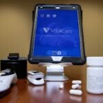 photo of iPad device, digital thermometer, and drug capsules on a table