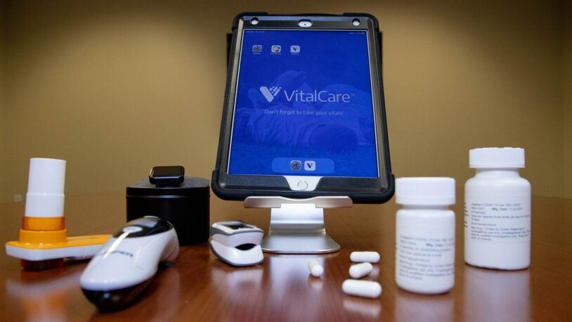 photo of iPad device, digital thermometer, and drug capsules on a table