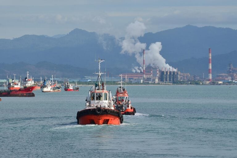 photo of a harbor with boats and factory with smoke stacks