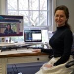 A photograph of Hannah Stewart, the Banbury Center's new Communications and Special Projects Coordinator. She is sitting in a black swivel chair and wearing a black turtleneck and cream skirt in front of a desk.