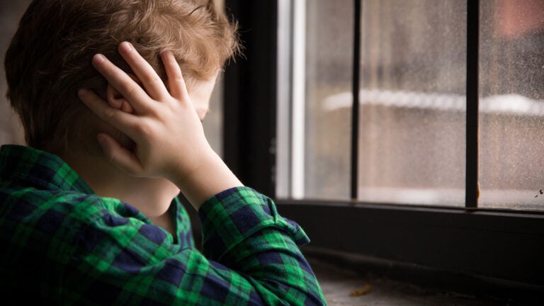 Photo of little boy standing behind the window in sad mood