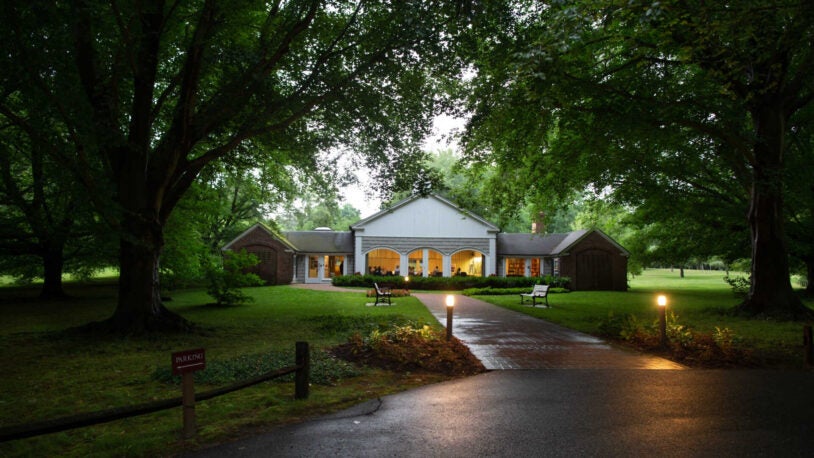 The outside of the Banbury Center during an autumn meeting in the mid-afternoon to evening. The conference room is illuminated and participants can be seen inside.