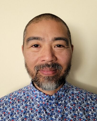 A photograph of Elvin Geng smiling. He is wearing a blue and white patterned shirt. 