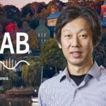image of Cold Spring Harbor campus from across the harbor with At the Lab podcast logo and portrait of Hiro Furukawa
