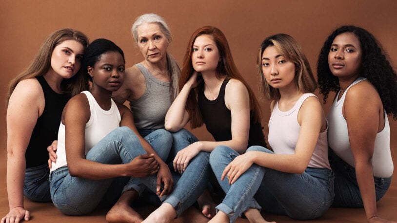 image of diverse women in casuals sitting on brown background. Multi-ethnic group of females looking at camera in studio.