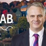 image of Cold Spring Harbor campus from across the harbor with At the Lab podcast logo and portrait of John Moses