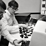 film still from Computer Chess film, 3 men sitting with chess boards and 1980s computers