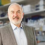 Adrian Krainer in front of shelves filled with laboratory equipment and supplies.