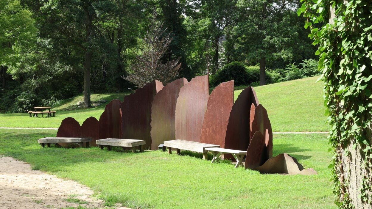 The Transform sculpture with curved panels and benches in a grassy park surrounded by trees.
