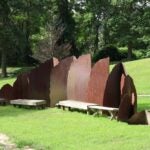 The Transform sculpture with curved panels and benches in a grassy park surrounded by trees.