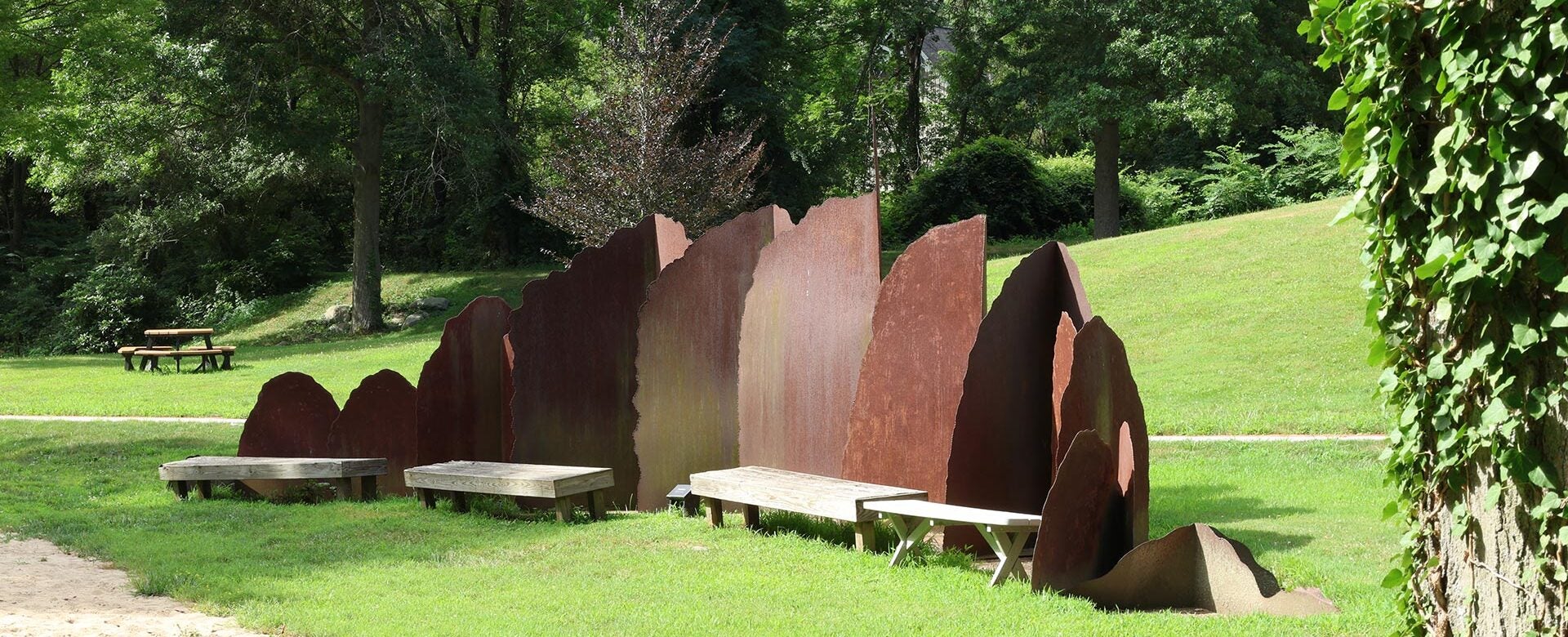 The Transform sculpture with curved panels and benches in a grassy park surrounded by trees.