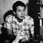 David Baltimore and Berwind Kaufmann examine scientific equipment; one is older with glasses, the other younger in a plaid shirt. Black and white.