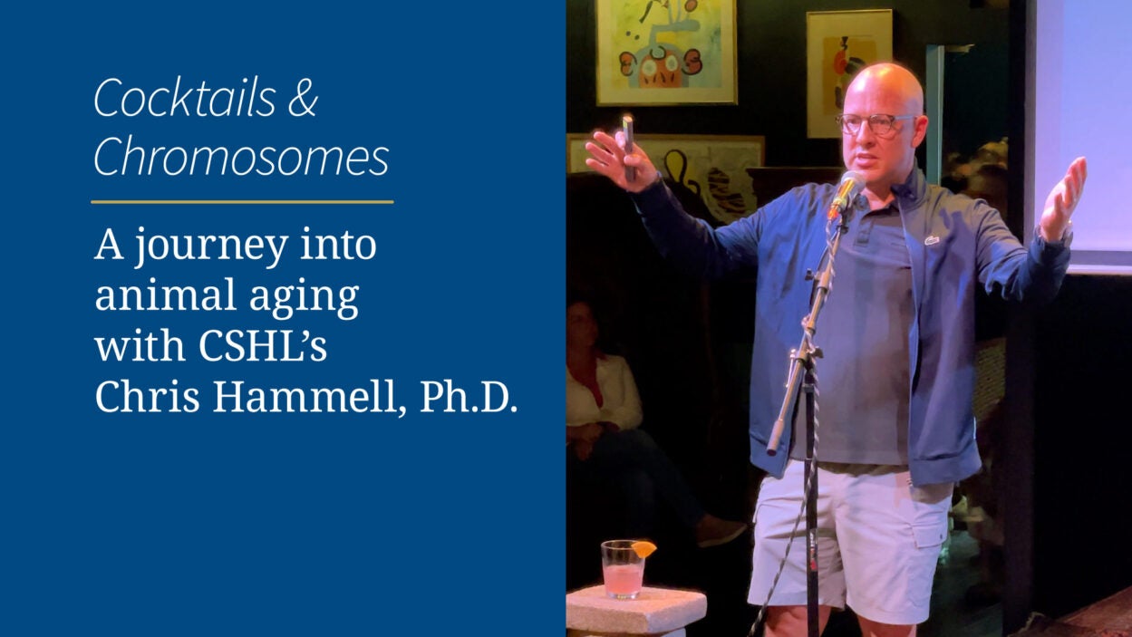 A man speaks passionately on stage next to a sign promoting a talk on animal aging by Chris Hammell, Ph.D.