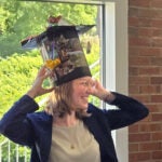 Leah Braviner indoors wearing a decorated graduation cap, hands touching the sides, sunlight in the background.