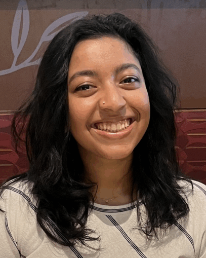 Ananya Sundararajan with dark hair smiling, wearing a white shirt with black stripes and a small nose stud.
