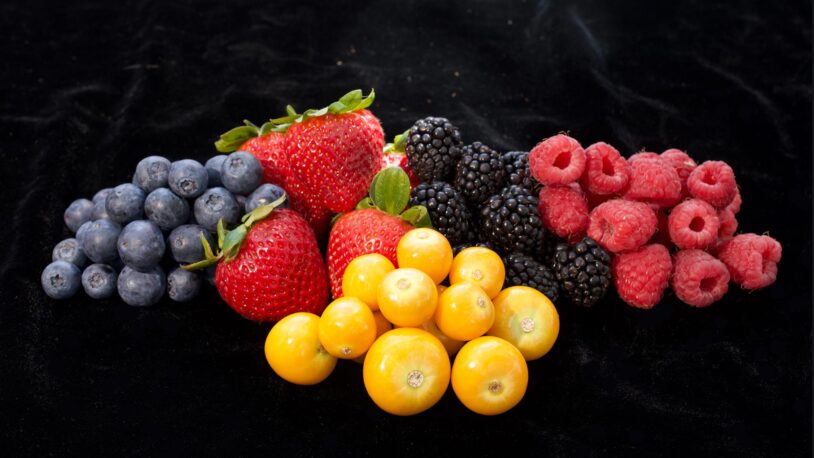Assorted berries and golden berries arranged on a black surface.